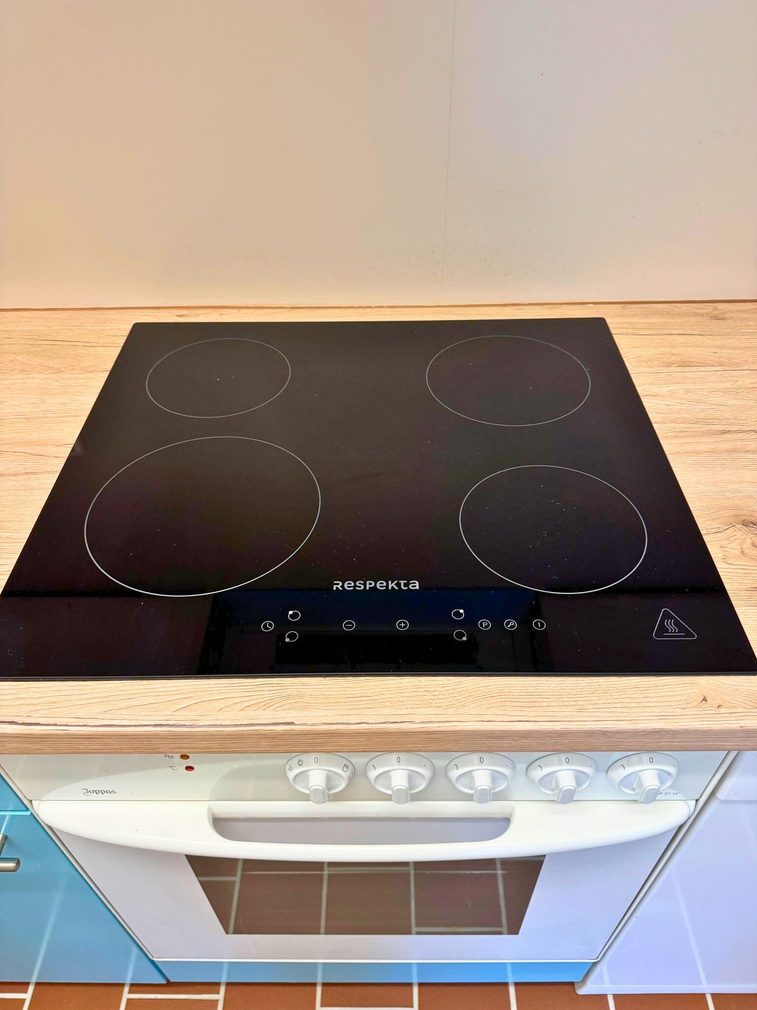 Een zwarte inductiekookplaat met vier branders en een bedieningspaneel, gemonteerd op een houten aanrecht boven een witte oven.