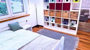 A bedroom with a bed, a white shelving unit with storage bins, a window with a view, and a grey sofa in the corner. - House with garden & private parking space in Cologne (Köln)