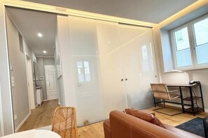 A modern room with a sliding glass door leading to a kitchen, a brown leather sofa, a small table with a chair, and a window with blinds.