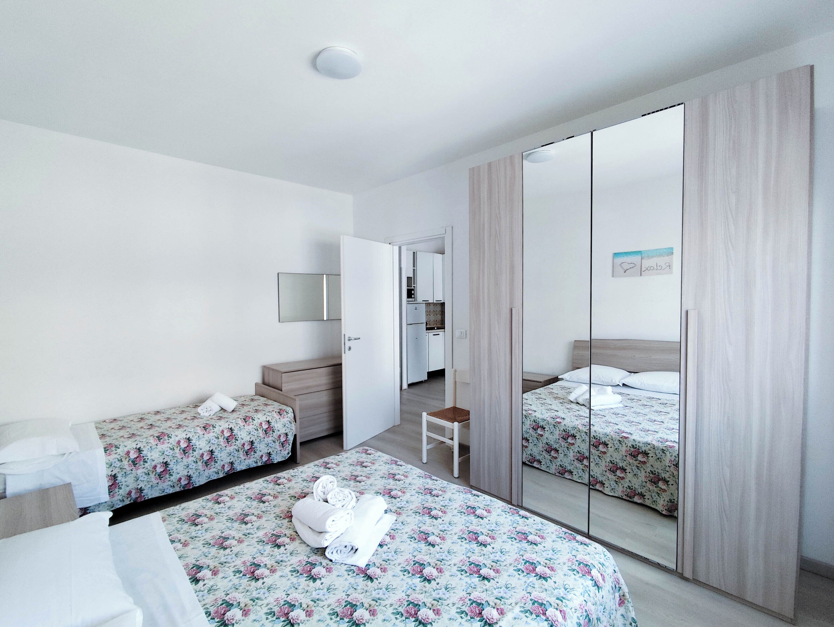Een hotelkamer met twee enkele bedden, een kleine tafel, een stoel, een spiegel en een kledingkast.