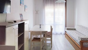 Een compacte, moderne woonruimte met een eettafel, stoelen, een bank en een aan de muur bevestigde televisie.