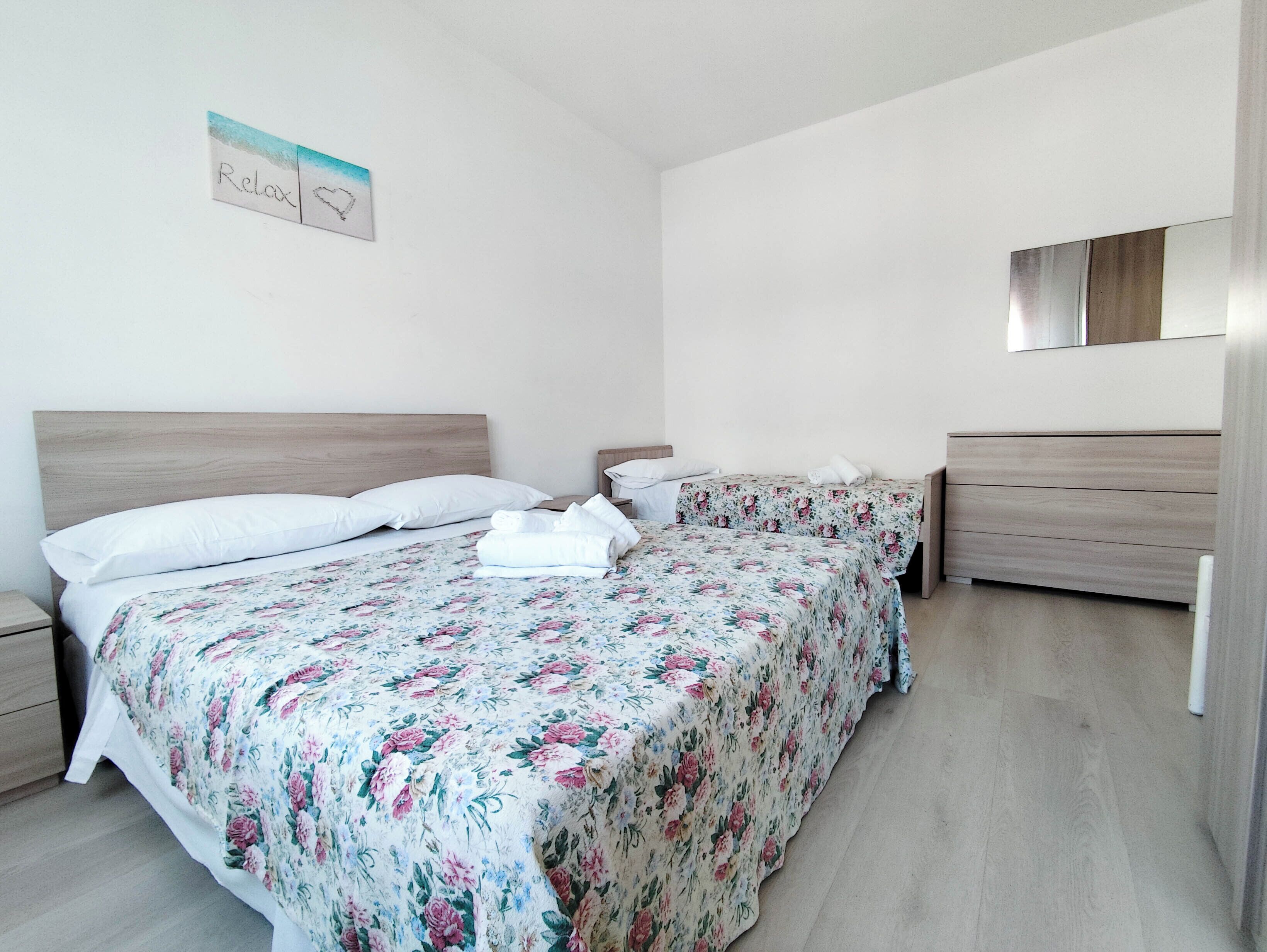 Une chambre d’hôtel avec deux lits, chacun agrémenté de draps à motifs floraux, de têtes de lit en bois et de tables de chevet blanches.