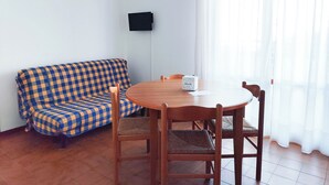 A room with a checkered sofa, a round wooden table, and a single chair. - Spacious Apartment With Balcony by the sea (Jesolo)