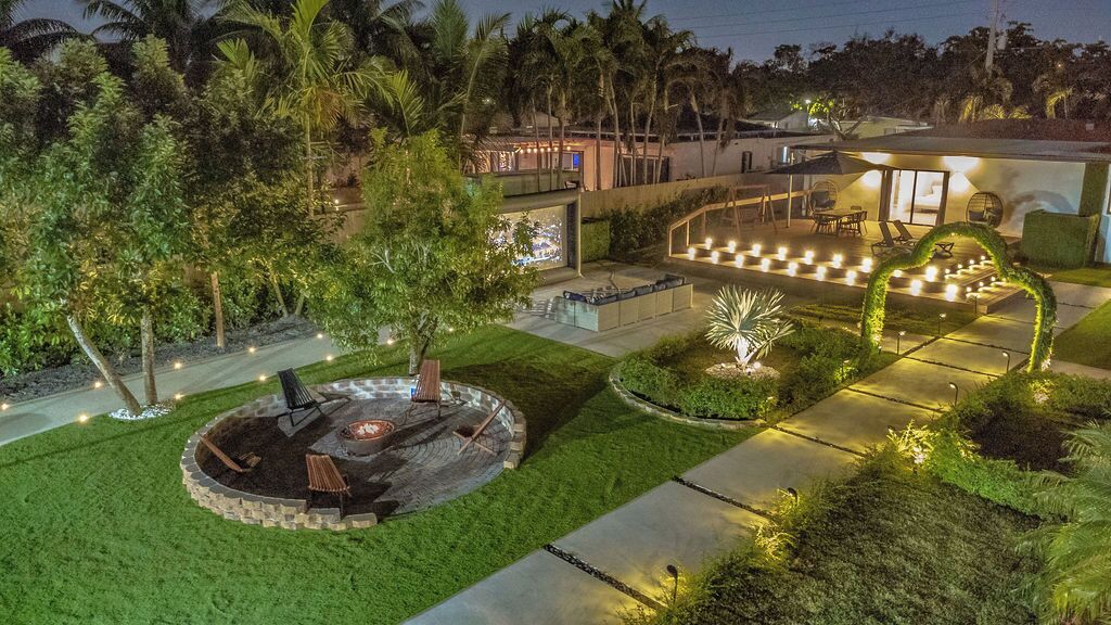 Un espacio exterior bien iluminado con una zona de estar circular, un brasero y una zona de comedor con mesas y sillas.