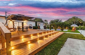 Une terrasse en bois avec des meubles d’extérieur, une balançoire et un patio bien éclairé.