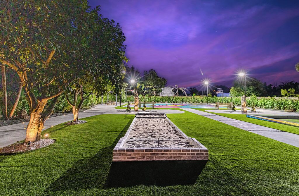 A landscaped garden with a rectangular water feature, trees, and street lamps.