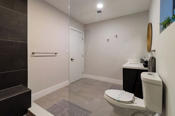 A modern bathroom with a glass shower enclosure, a white toilet, and a black sink.