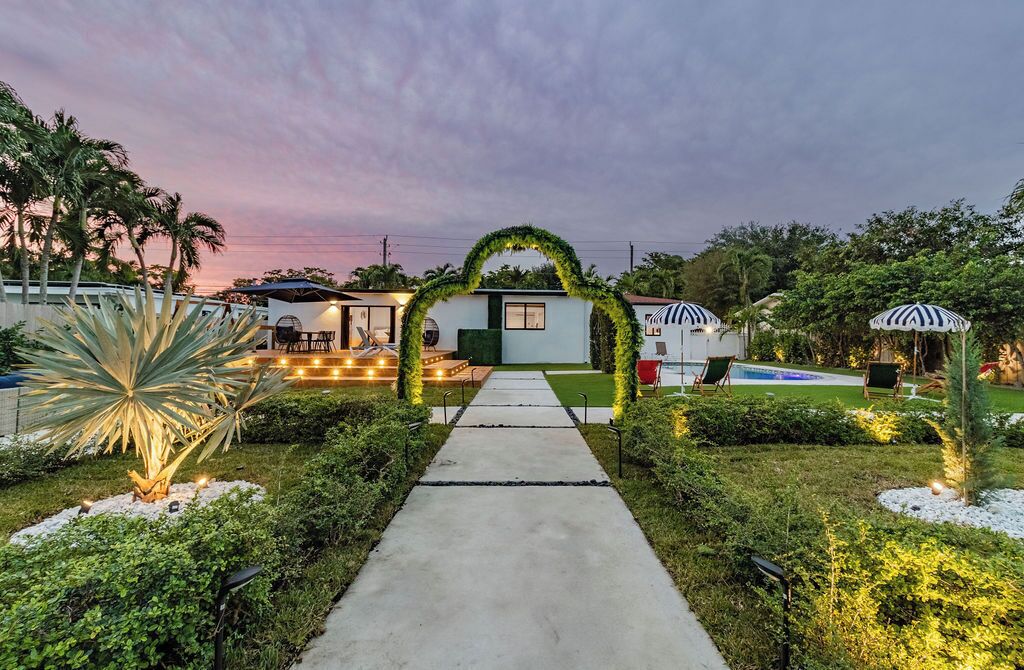 Un camino conduce a un edificio con un arco verde, rodeado de jardines cuidados y zonas de estar al aire libre.