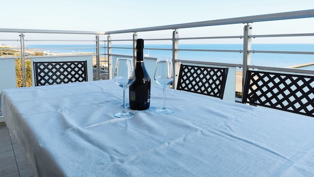 A table with a bottle and two glasses on a balcony overlooking the sea. - Spacious Flat With Balcony by the sea (Jesolo)