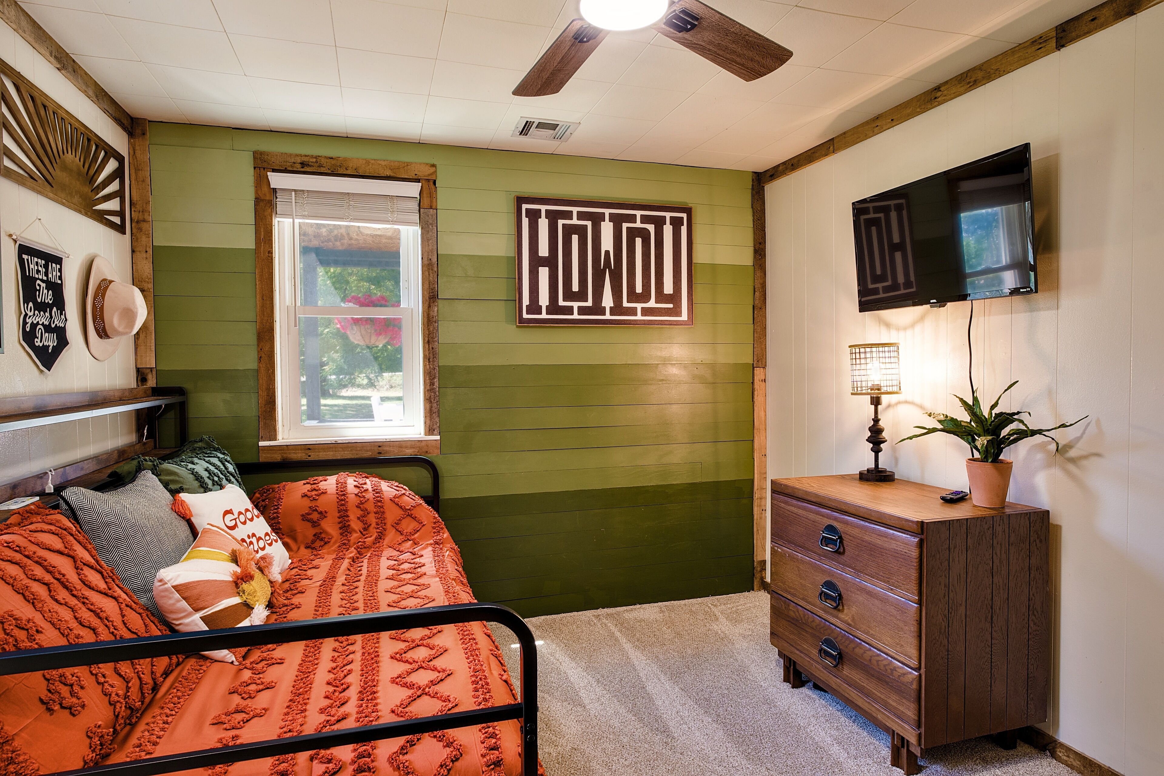 A room with a bed, a dresser, a TV, and a window with a view of greenery.