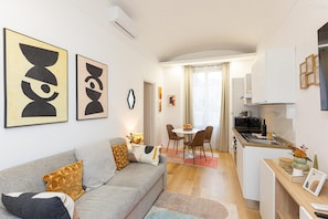Eine moderne Wohnung mit Wohnzimmer, Essbereich und Küche. An den Wänden befinden sich abstrakte Gemälde, ein Sofa mit Kissen und ein Esstisch mit Stühlen.
