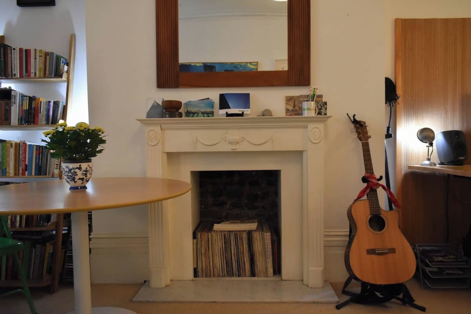 Une pièce avec une cheminée, des étagères à livres, une guitare et une table sur laquelle est posée une plante en pot.