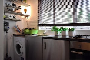 Cozinha com máquina de lavar, pia e janela com persianas.