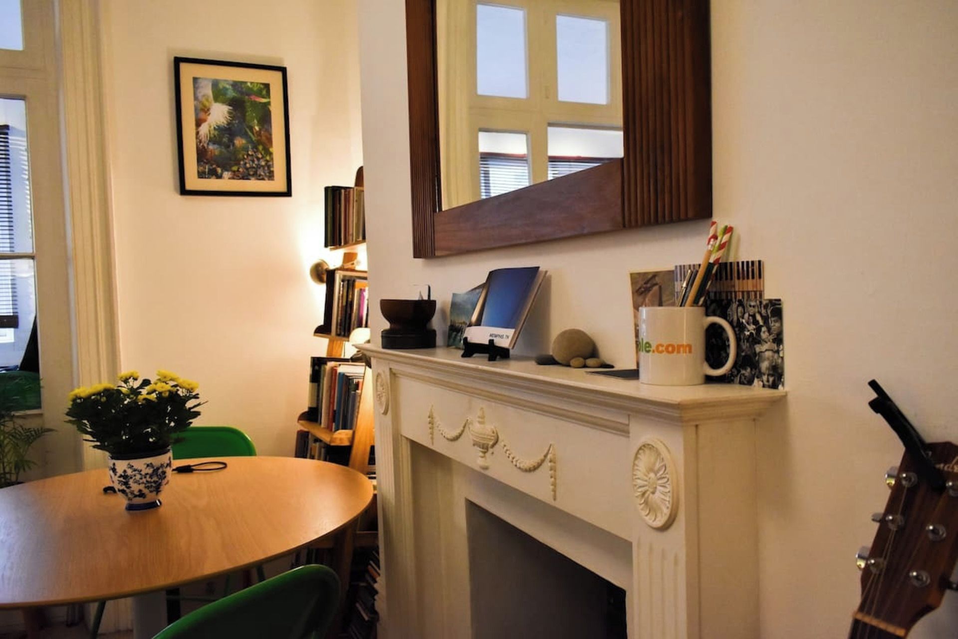A room with a fireplace, a table with chairs, a bookshelf, and a framed picture on the wall.
