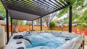 Een hottub onder een pergola, met een houten hek en buitenstoelen op de achtergrond.
