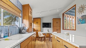 Een moderne keuken met houten kastjes, een wit aanrecht en een eethoek met een tafel en stoelen.