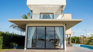A modern two-story house with a large glass door, a pool, and wind turbines in the background. - Villa Eivissa Dunes (Trairi)
