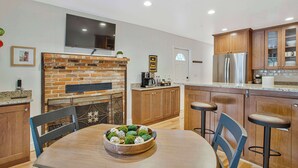 Una cocina moderna con chimenea de ladrillo, armarios de madera y un televisor grande montado encima.