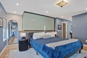 A bedroom with a large bed, bedside tables, a mirror, and a ceiling light fixture. - Luxe Row Home Steps to USNA Gate 3! (Annapolis)
