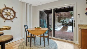 Un comedor con una mesa y sillas de madera, un adorno de timón de barco en la pared y vistas a un jardín nevado a través de un ventanal corredero.