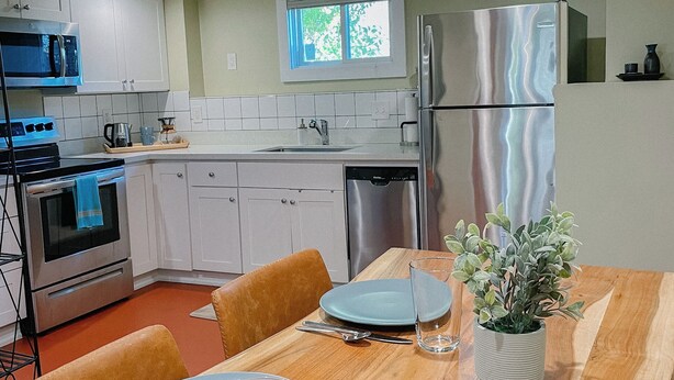 A modern kitchen with white cabinets, stainless steel appliances, and a wooden dining table set for two. - Quaint 1-bedroom house in Ballard neighborhood of Seattle for a perfect getaway (Seattle)