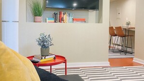 A living room with a flat-screen TV mounted on the wall, a red coffee table with books and a plant, a black sofa, and a checkered rug. - Quaint 1-bedroom house in Ballard neighborhood of Seattle for a perfect getaway (Seattle)