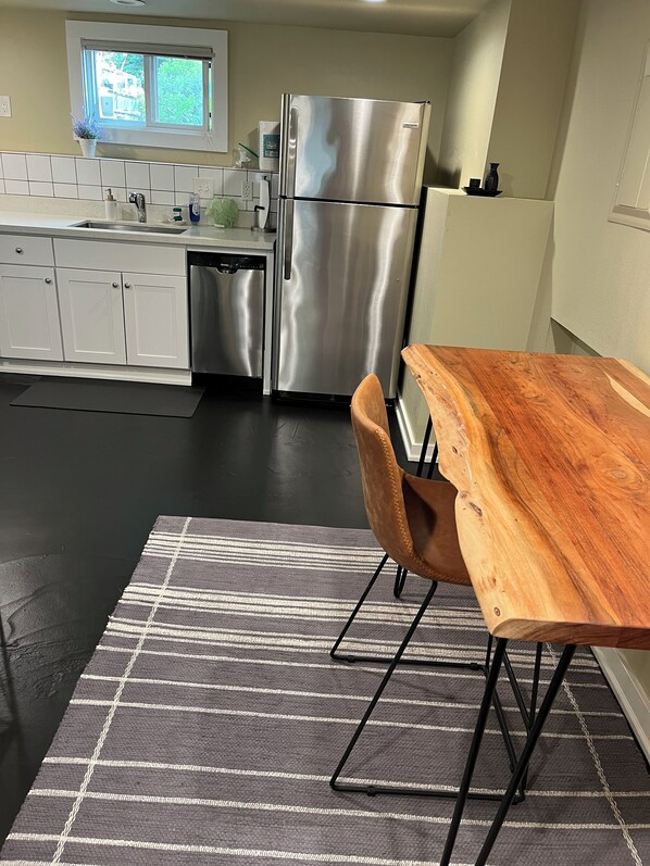 Et moderne køkken med et rustfrit stål køleskab, hvide skabe og et træ spisebord med stole.