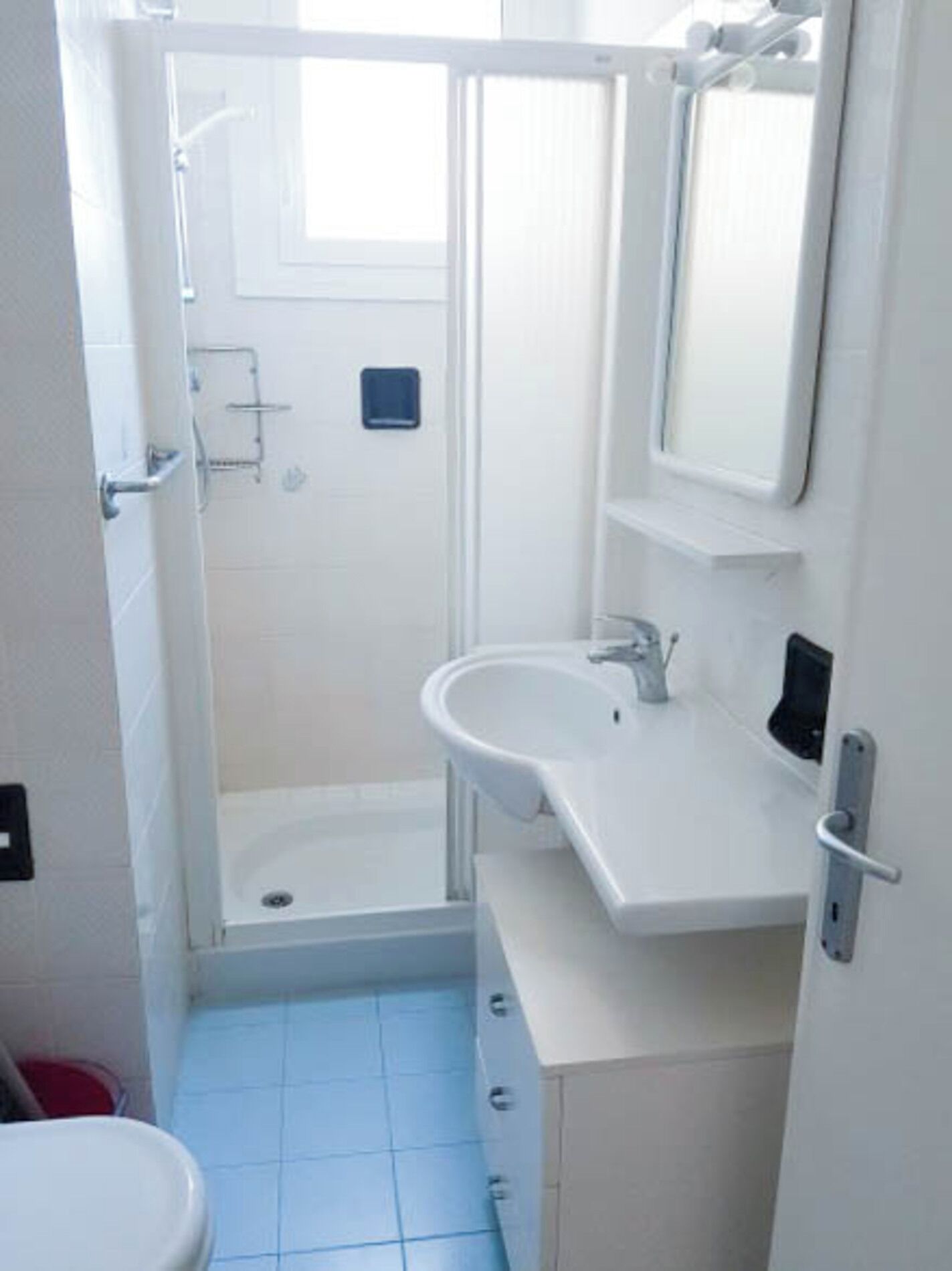 A small, white bathroom with a sink, mirror, and shower.