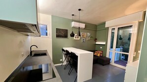 Una cocina compacta con una isla central, un comedor con sillas, un sofá y un puerta corrediza de vidrio que da a un balcón.