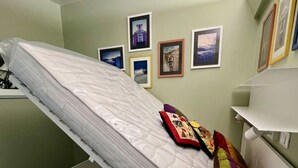 Una habitación con una cama en diagonal, una mesita de noche blanca y una pared con cuadros enmarcados.