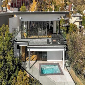 Une maison moderne à deux étages, dotée d’une façade en verre, d’une terrasse sur le toit et d’une piscine.
