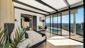Une chambre moderne avec un grand lit, une télévision et une vue sur les toits de la ville et la piscine.