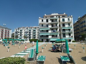 Ein Strandhotel mit mehreren Balkonen, Liegestühlen und Sonnenschirmen.