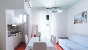 A compact living space with a dining area, kitchenette, and a light-colored sofa. - Comfy Apartment With Pool Access (Jesolo)