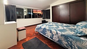 Een slaapkamer met een bed, een raam met gordijnen, een houten vloer en een kledingkast.
