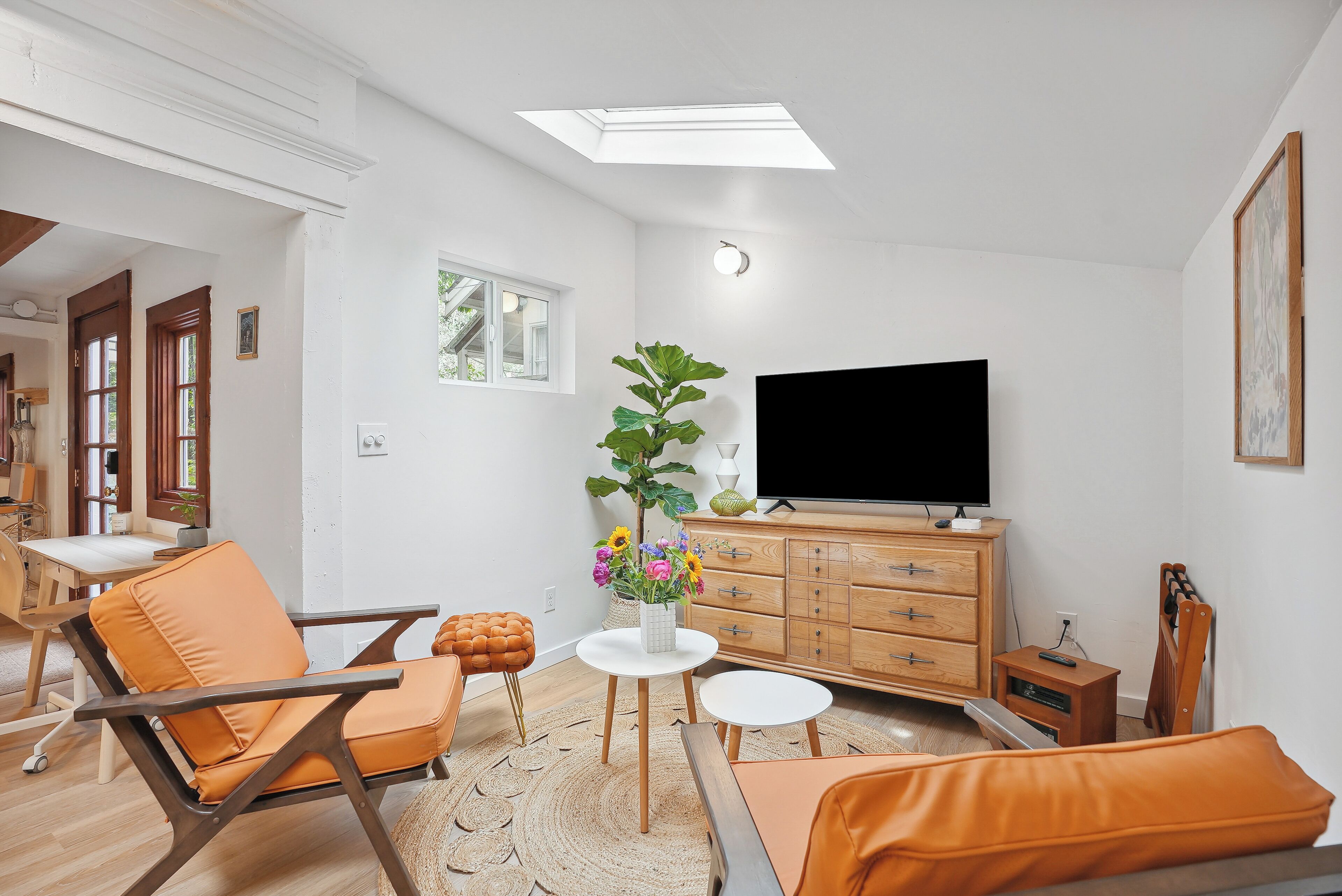 A modern living room with a flat-screen TV, wooden furniture, and a large window.