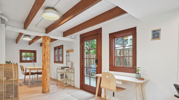 Una habitación con vigas de madera, un escritorio, una silla, una mesa de comedor y una ventana con vistas a zonas verdes.