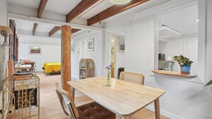 Un comedor con una mesa de madera, sillas con cojines marrones, un carrito metálico y un mantel amarillo.