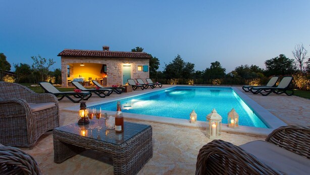 Ein Pool mit Liegestühlen und einem Tisch, umgeben von Steinböden und einem Gebäude mit einem Ziegeldach.
