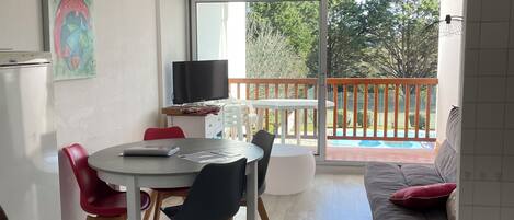 A modern living space with a dining area, a sofa, and a balcony with a pool view.