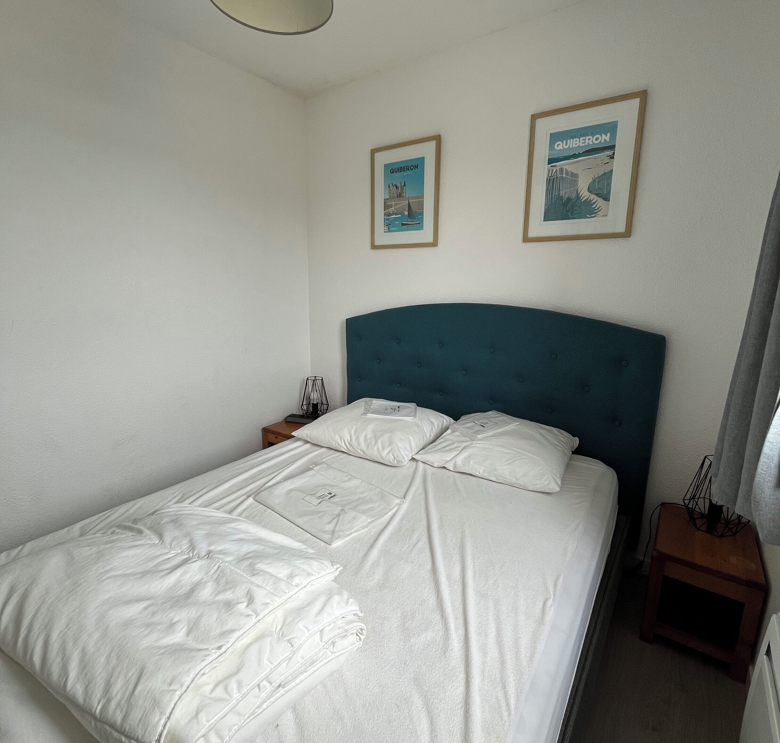 A neatly made bed with white linens, a blue headboard, and two framed pictures on the wall.