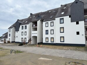 Ein mehrstöckiges Wohngebäude mit flachem Dach, zahlreichen Fenstern und einer Treppe, die zu einer oberen Etage führt.