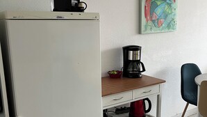 Una cocina compacta con un refrigerador blanco, una cafetera sobre una mesa de madera y un hervidor rojo.