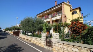 Una casa de dos pisos con balcón, pared de piedra y una calle al frente.