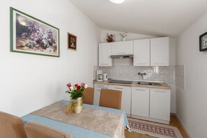 A compact kitchen with white cabinets, a coffee maker, and a sink. There is a dining table with a vase of flowers and a rug. - Comfortable flat just 600 metres from the beach and UNESCO World Heritage Site (Porec)
