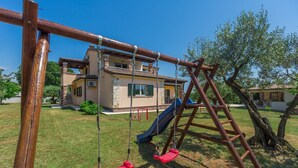 Ein Schaukelgestell aus Holz mit Rutsche, einer Leiter und einem Haus im Hintergrund.