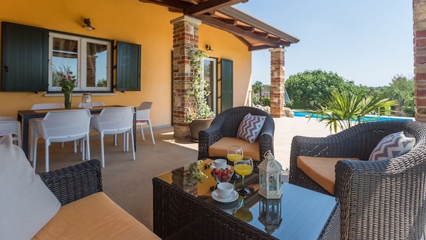 Eine Terrasse im Freien mit Korbmöbeln, einem Esstisch und Blick auf einen Swimmingpool.