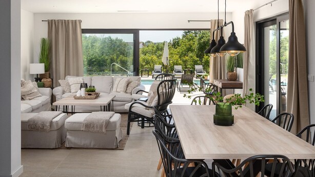 Ein modernes Wohnzimmer mit einer Sofagarnitur, einem Esstisch und Stühlen. Ein großes Fenster bietet einen Blick ins Freie.