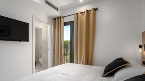 Ein Schlafzimmer mit einem Bett, einem an der Wand montierten Fernseher und einem Fenster mit Vorhängen.