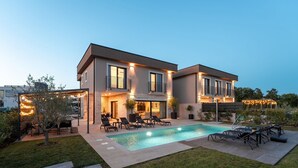 Ein modernes, zweistöckiges Haus mit Swimmingpool, Sitzgelegenheiten im Freien und Lichterketten.